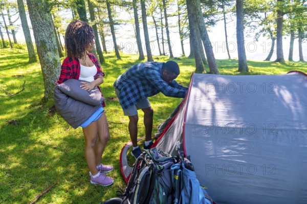 Couple setting up a tent in a lush forest, preparing their campsite for a summer adventure filled