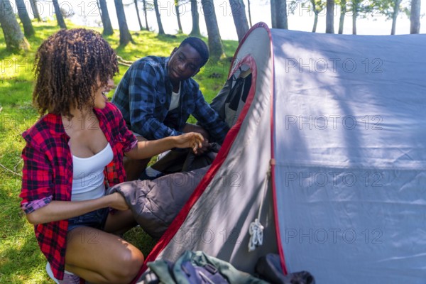 Young black couple enjoying the outdoors while setting up a camping tent in the forest, placing a