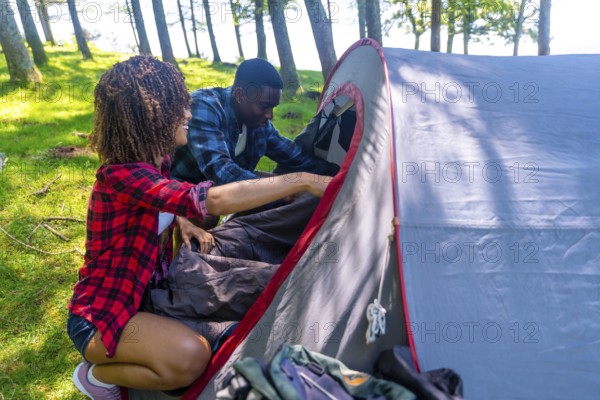 Hikers are setting up camp in the forest, putting sleeping bags inside their tent on a beautiful
