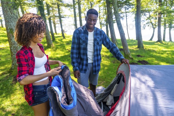 Young black couple setting up their tent in a forest campground near a lake, enjoying a summer