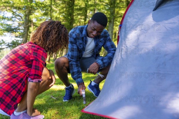 Young black couple setting up their tent in a serene forest, embracing the joy of camping and
