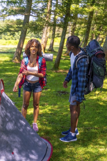 Young couple setting up their campsite while enjoying a backpacking adventure in the lush woods,