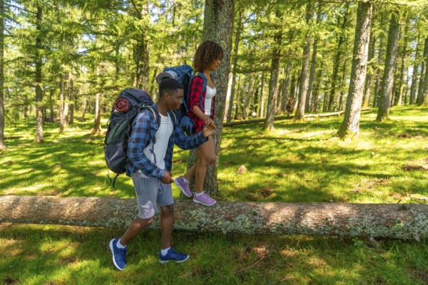 Young backpacking couple carefully balancing on a fallen tree trunk while hiking through a lush