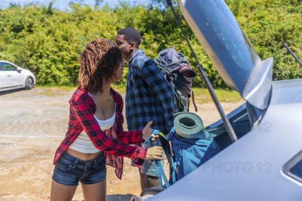 Young couple unpacking their backpacks from the trunk of the car, excitedly preparing for an