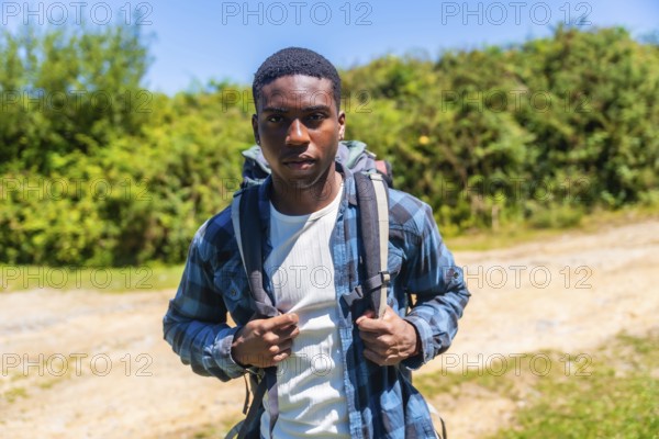 Confident young hiker wearing a backpack, enjoying a sunny day while discovering a beautiful nature