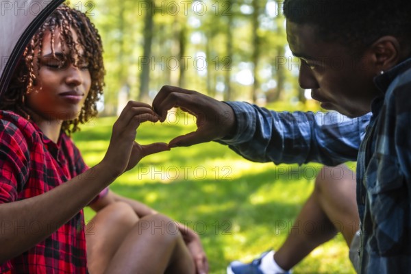 Happy couple making heart shape with hands while camping in nature, enjoying a romantic moment