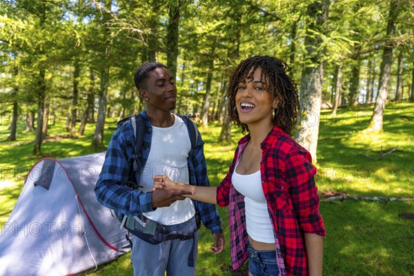 Happy smiling backpackers holding hands near tent in the woods, enjoying summer vacation camping