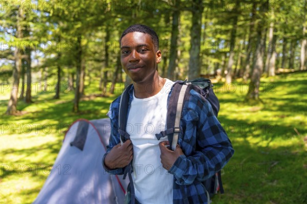 Young black man wearing a backpack, enjoying a camping trip in the woods, surrounded by lush trees