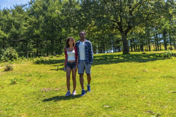 Young multi ethnic couple enjoying a sunny summer day, walking hand in hand through a lush green
