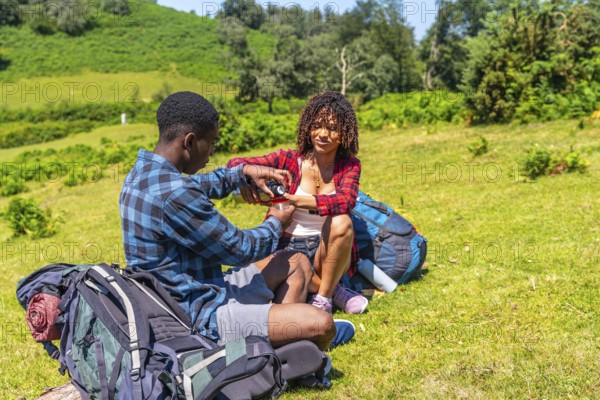 Young couple of hikers taking a break on a grassy hillside, sharing refreshments from a thermos