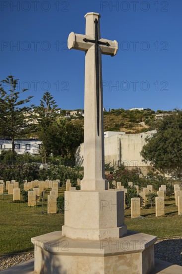 A high stone cross in a well-kept peaceful military cemetery under a clear blue sky, Military