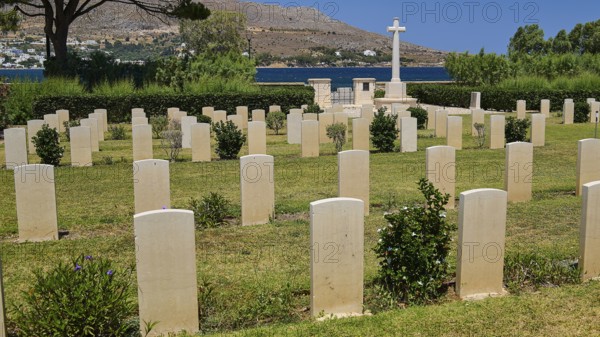 Cemetery with many gravestones in front of mountains and sea under blue sky, Military Cemetery,