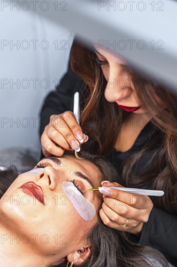Beautician carefully applying individual false eyelashes on client's upper eyelid using tweezers in