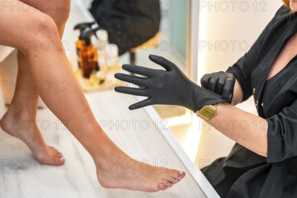 Beautician putting on black gloves, preparing for a beauty treatment on a client's legs in a beauty