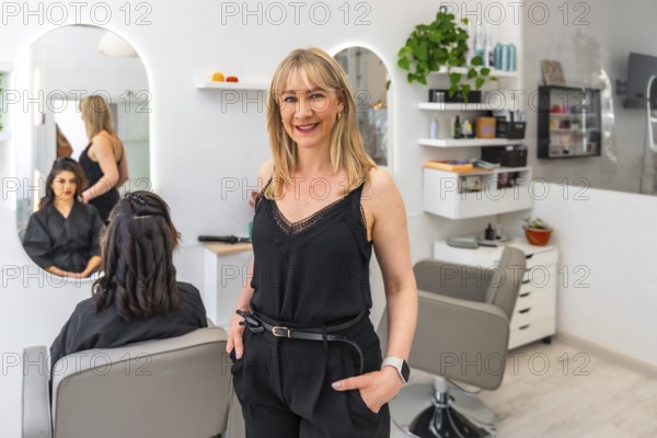 Confident female entrepreneur stands with hands in pockets, managing her modern hair salon, while a