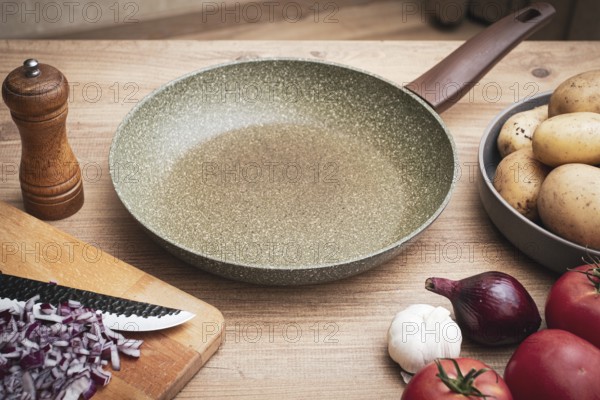 Fresh ingredients including potatoes, garlic, tomatoes, and onions are arranged on a wooden table