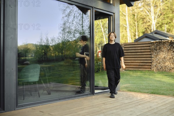 Two boys are walking out of a sleek, contemporary house showcasing large glass doors. The
