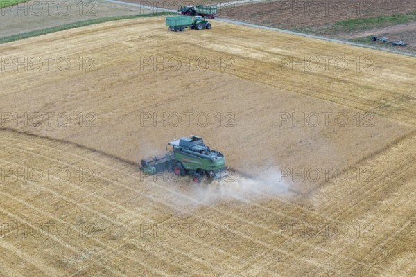 Harvesters harvesting a wide field surrounded by dust, tractors, basket in the Rems Valley,