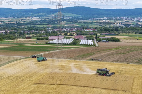 Wide fields with combine harvesters and tractors against a backdrop of mountains and a power pole,