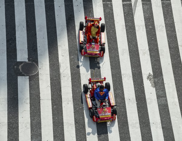People in costumes drive small go-kart racing cars across zebra crossings, Shibuya Crossing,