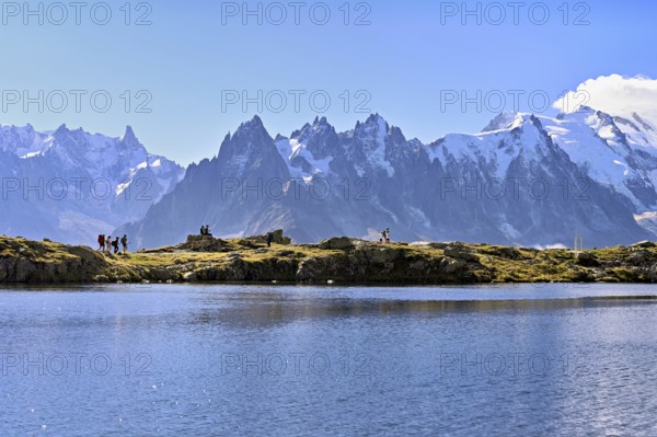 A group of hikers at Lac de Chésserys, behind the snow-covered Mont Blanc massif,