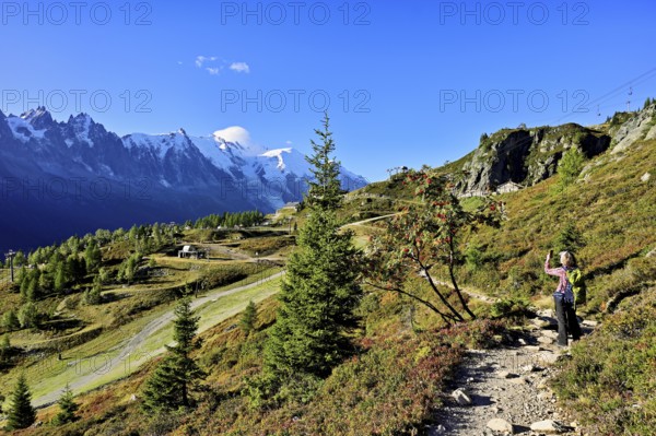 Female hiker on a hiking trail with the La Flégère cable car mountain station and the snow-covered