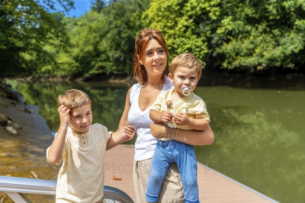 Mother holding her baby while walking alongside her other son on a picturesque pier, enjoying a