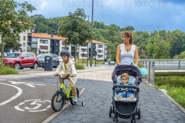 Mother pushing a baby stroller while her son rides a bicycle on a bike path in a modern urban