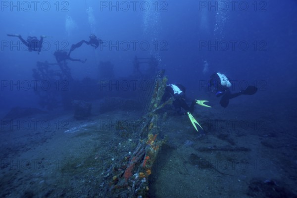Divers explore a wreck covered with sea sponges on the ocean floor in deep blue water in the