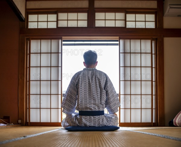 Young man wearing kimono sitting in traditional Japanese living room with tatami mats and shoji