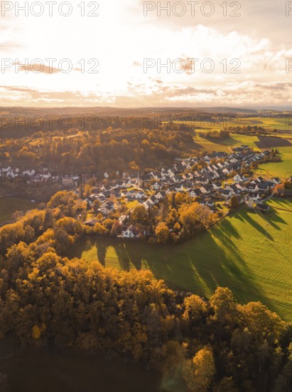 Autumn landscape with a village flooded with warm light, surrounded by fields and forests,