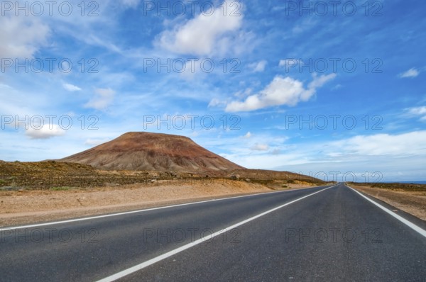 View of long straight paved road to the left partly eroded volcano volcanic cone in volcanic