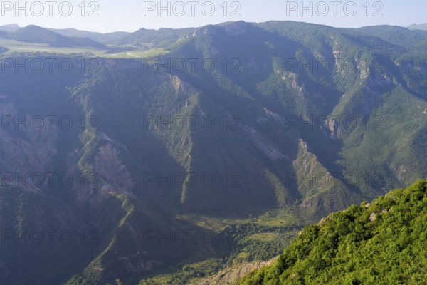Green, wooded mountain slopes in the sun surrounding vast valleys, view of the Vorotan River
