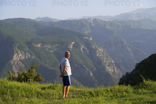 Man standing in a green field with a view of majestic mountain landscape and valley of the Vorotan