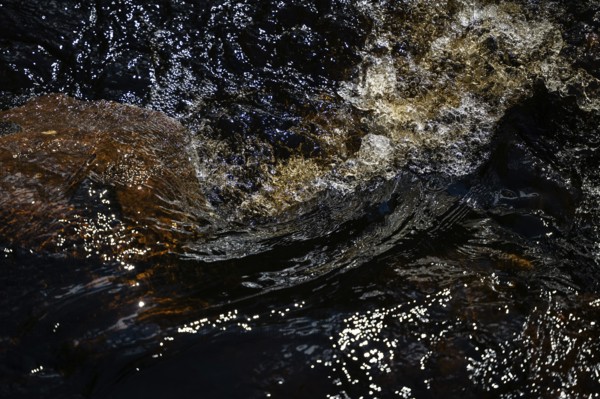 Stream flow with dark water, reflections of light and turbulence, Sweden
