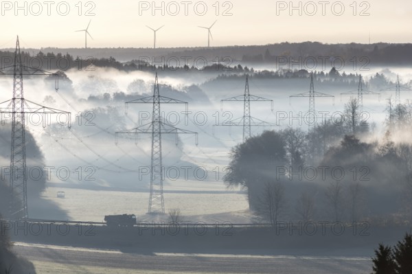 Misty morning landscape with power poles in the foreground and wind turbines, Swabian Jura,