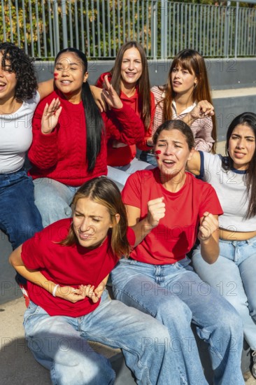 Group of diverse young women friends wearing red shirts and face paint, sitting together and