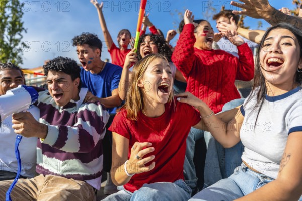 Diverse group of young adult sports fans cheering and shouting with arms raised in stadium stands,