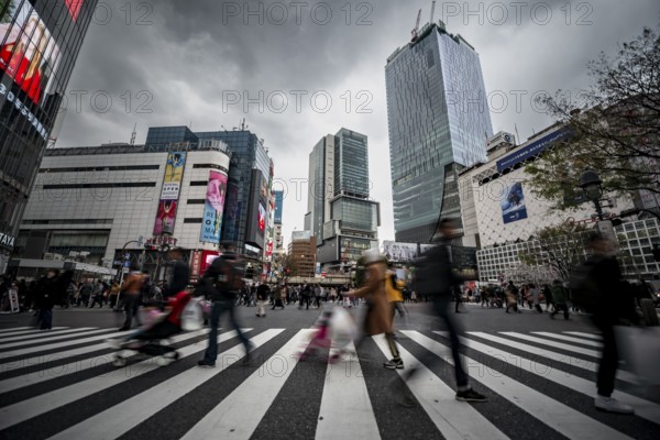 Crowd crossing zebra crossing on a large intersection, motion blur, back modern houses with