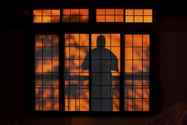 Shadows of a man in kimono, on the balcony behind sliding shoji doors in a traditional Japanese