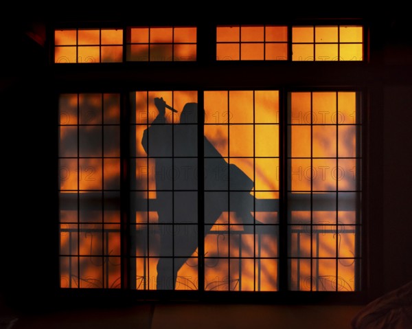 Shadow of a man, burglar with knife, assassin, ninja, on the balcony behind sliding shoji doors in