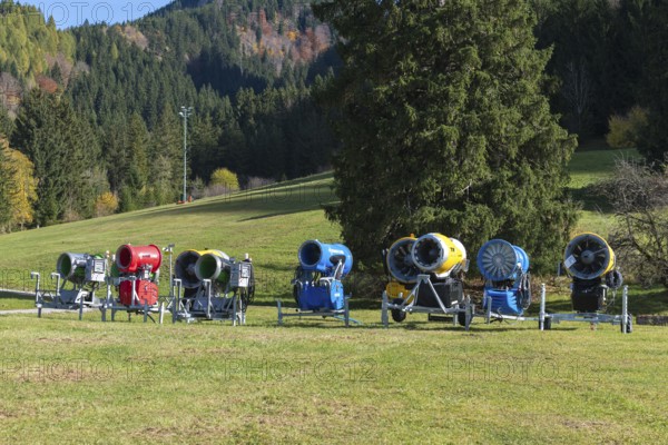 Different snow cannons on an extensive meadow in front of a forest in autumn, Schwangau near