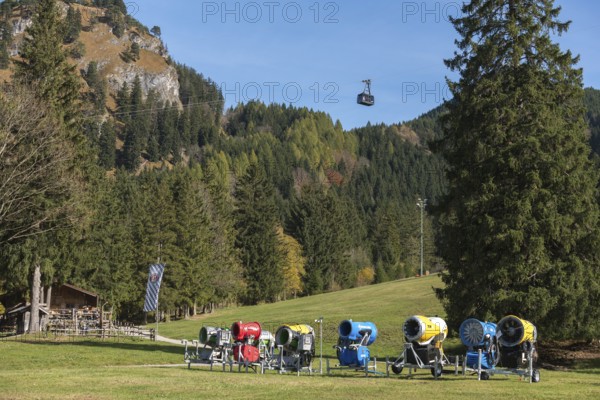 Snow cannons in front of a forest, mountains in the background, Tegelbergbahn cabin floating,