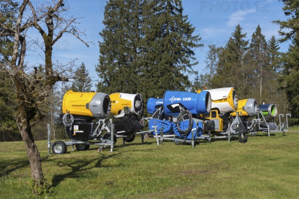Row of snow cannons in a meadow with trees and partly cloudy sky, Schwangau near Füssen, Ostallgäu,