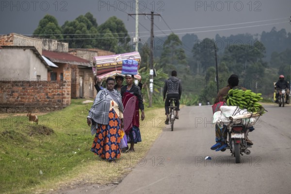 Street scene in rural Uganda, woman carrying bags and mattresses on their heads, motorcyclists