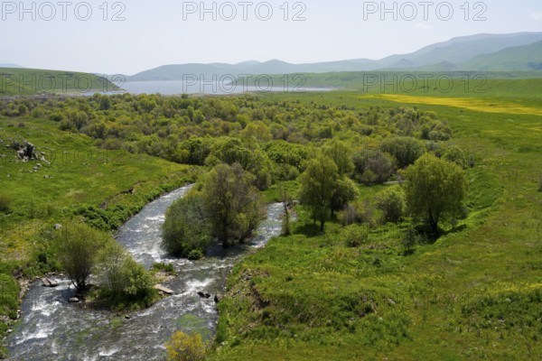 A river flows through a landscape of green trees and hills, Vorotan River, Vorotan, in the