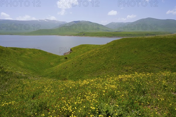 Green hills surround a calm lake under blue sky, spring-like atmosphere, Spandaryan Reservoir,