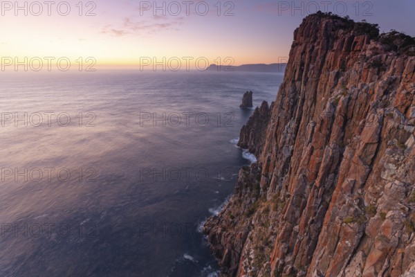 Long exposure at sunrise shows glowing dawn over the dramatic rocks on the Cape Hauy Track. Gentle