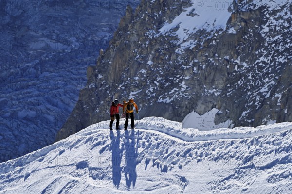 Two ascended mountaineers run across a snow-covered mountain ridge, Aiguille du Midi,