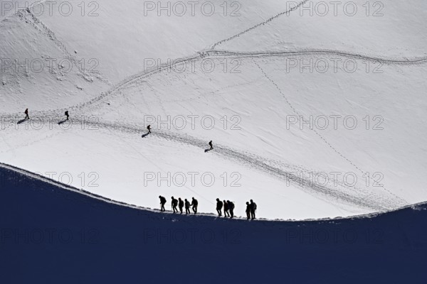 A group of mountaineers runs across a snow-covered mountain ridge, Aiguille du Midi,
